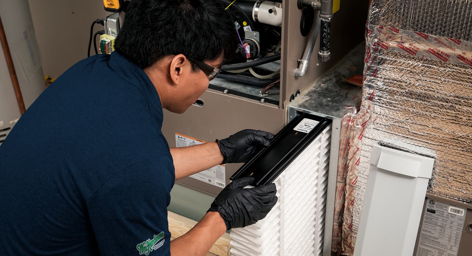 A professional Wm Henderson HVAC technician replacing a clean pleated air filter in an indoor air handler unit during a routine AC maintenance tune-up.