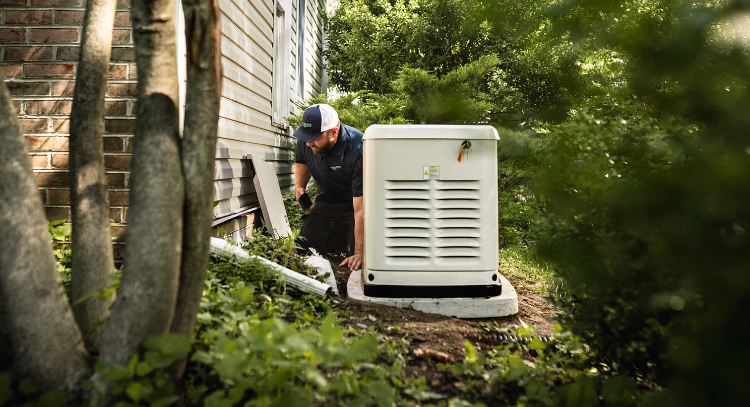 A professional technician inspects a large, beige whole-home standby generator installed on a concrete pad outside a residential house.