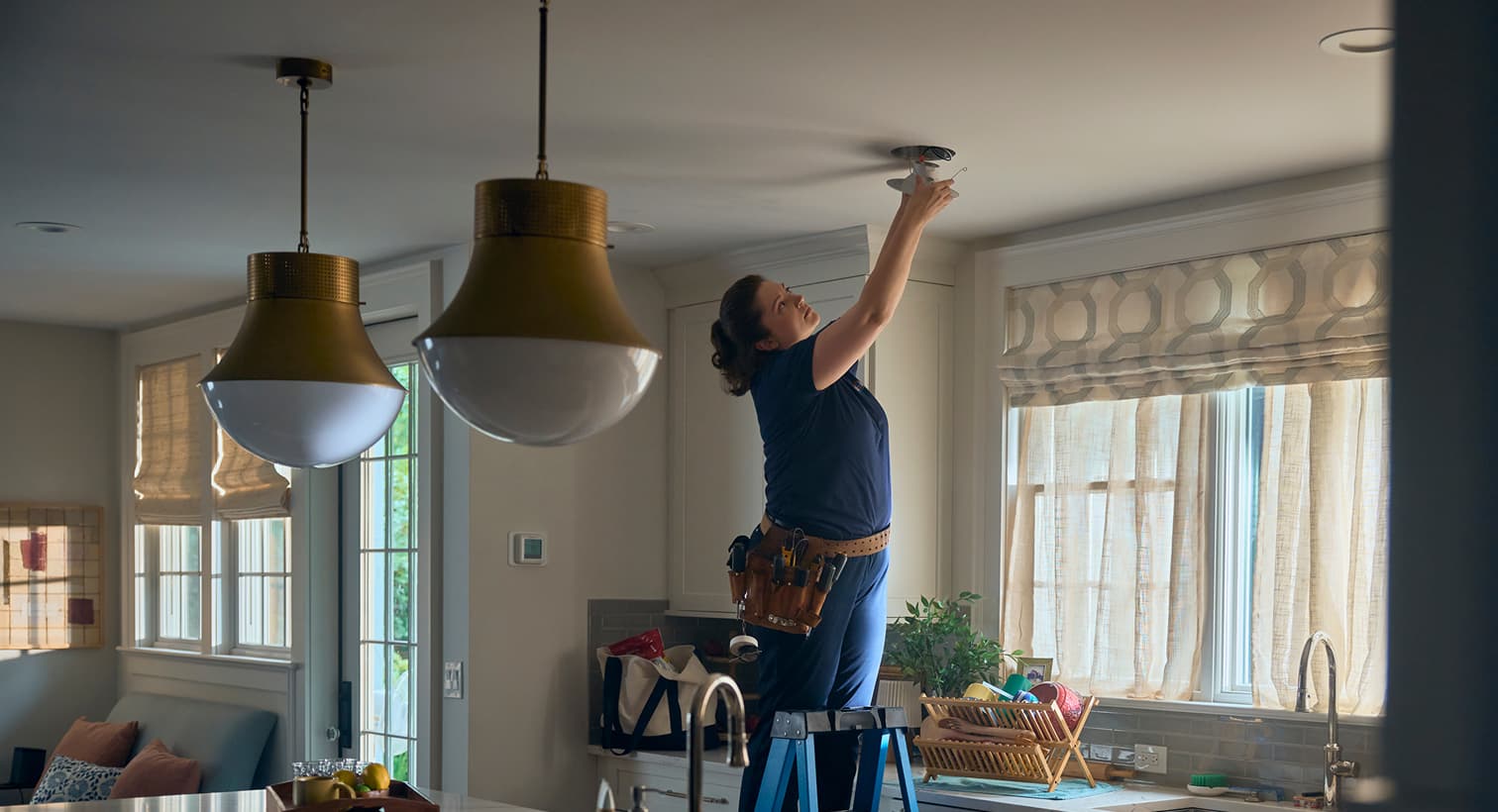 A professional Wm Henderson electrician standing on a ladder to install modern recessed ceiling lights during a residential electrical installation service.