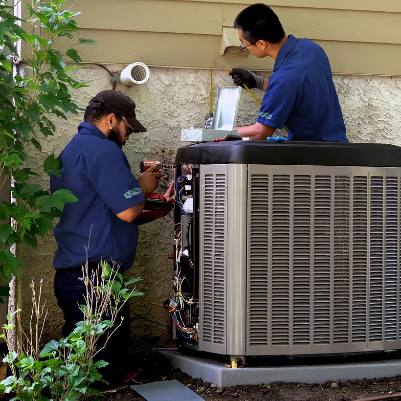 Two Wm Henderson HVAC technicians installing a brand-new residential outdoor air conditioning condenser unit during a home AC replacement service.