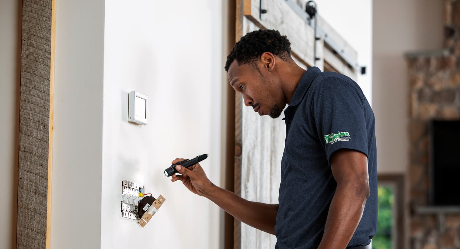 A professional Wm Henderson electrician using a flashlight to safely inspect and troubleshoot exposed residential wall switch wiring during an electrical repair service.